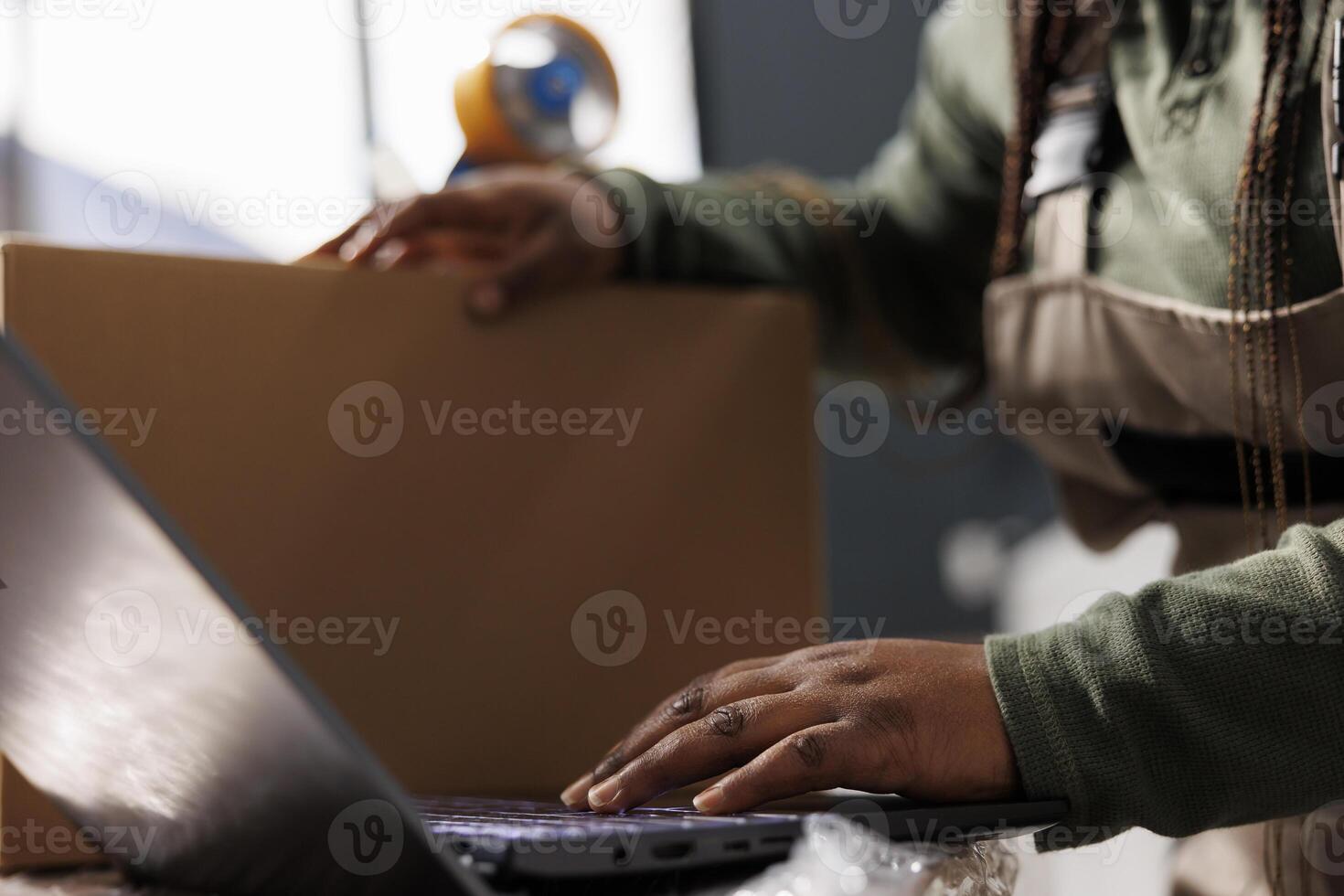 Close up of storehouse employee analyzing goods logistics on laptop computer, working at merchandise quality control report in storage room. African american supervisor preparing customers orders photo