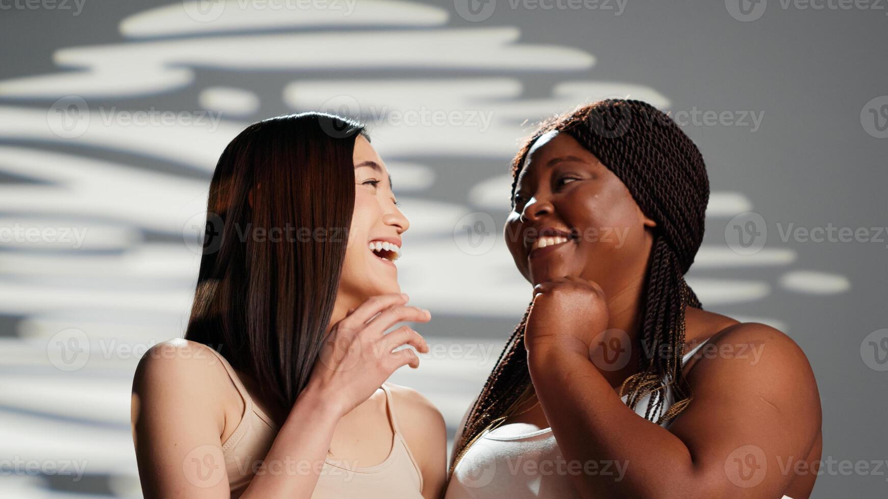 African american model whispering secret with friend, creating skincare and femininity campaign. Advertising body positivity and self love in studio, diverse women laughing. Beautiful girls. photo