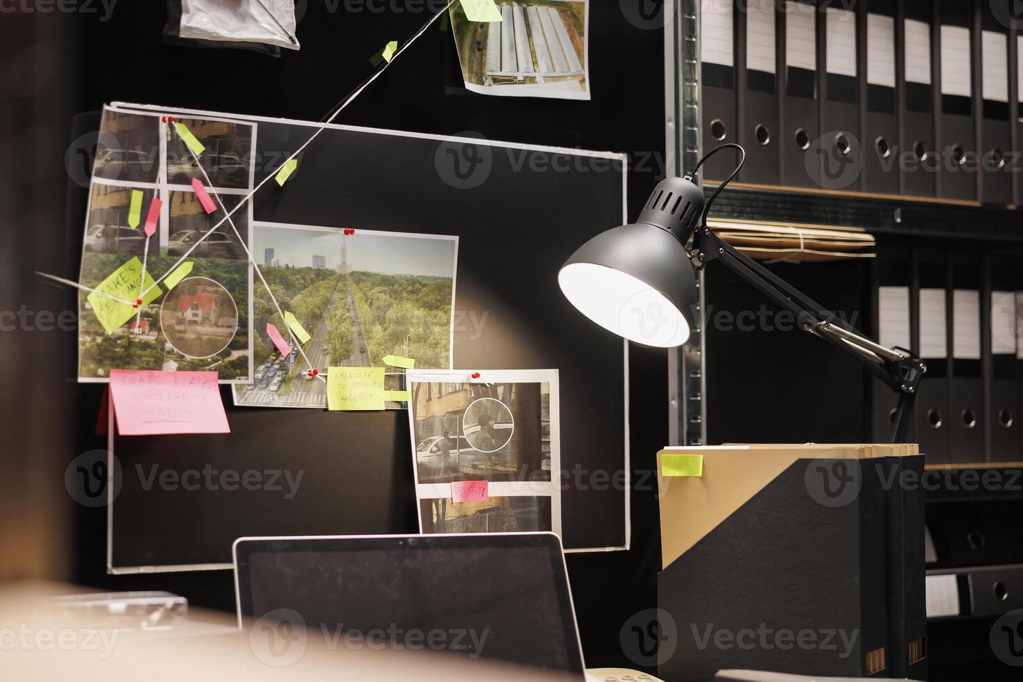 Crime evidence board with investigation process map lit with desk lamp in private investigator room. Police detective gathered information hanging on wall and table with laptop in office photo