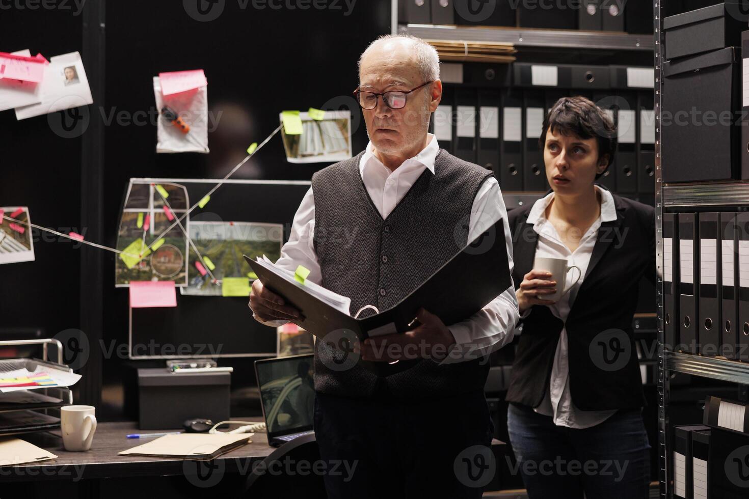 Private detectives working at criminal case, analyzing crime scene evidence in arhive room. Police officer checking confidential federal files, discussing investigation report with investigator photo