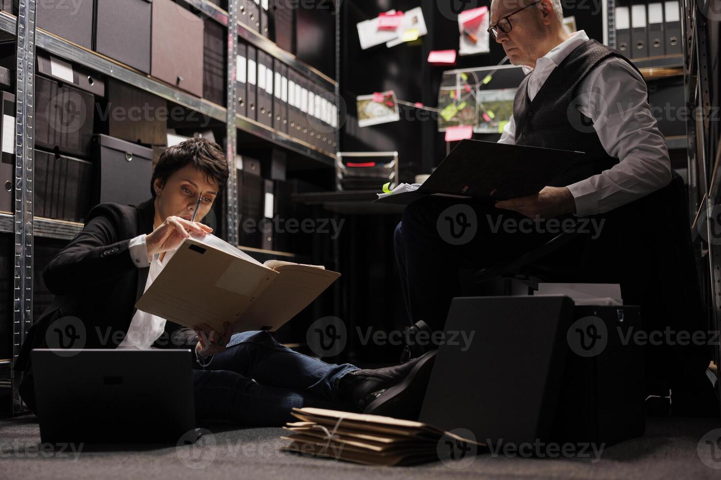 Tired police officers holding files with crime scene evidence, analyzing criminology report in arhive room. Overworked private detectives working late at night at missing person case photo
