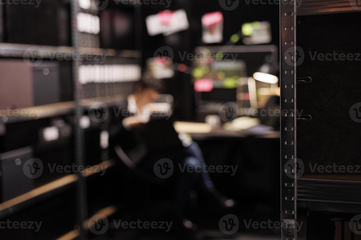 Selective focus of shelves full with evidence files, in background private investigator reading crime scene report. Police officer working late at night at missing person case in arhive room. photo