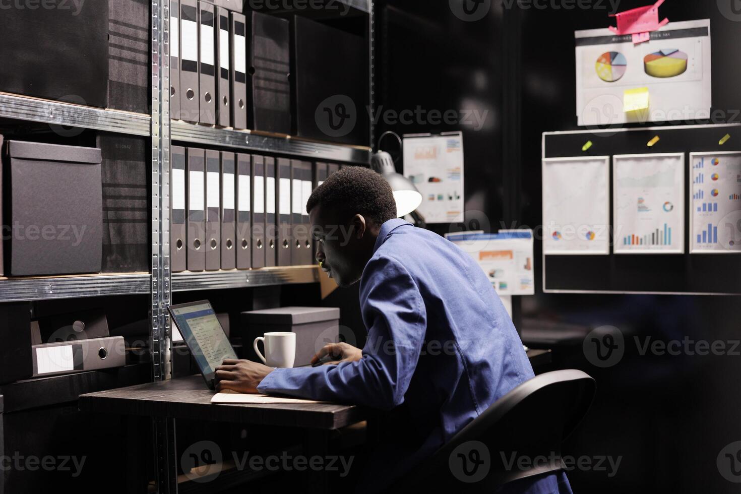 Police officer reading police investigations report, analyzing crime evidence trying to catch mysterious suspect. African american private detective checking victim files in arhive room photo