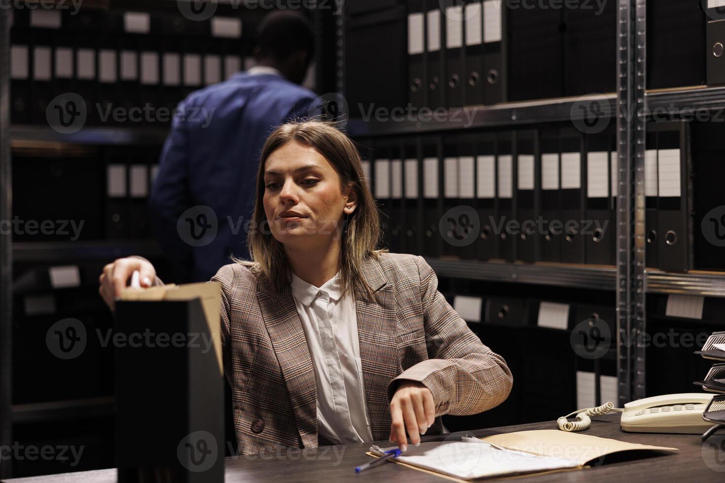 Businesswoman searching corporate files, working late at night at accountancy report in storage room. Caucasian manager analyzing bureaucracy record, reading administrative documents photo