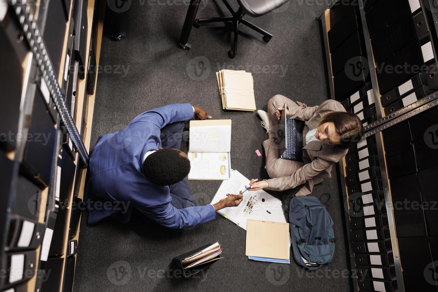 Top view of diverse inspectors working at fraude cause, analyzing company evidence trying to catch suspect in arhive room. Private detective discussing criminology report during investigation photo