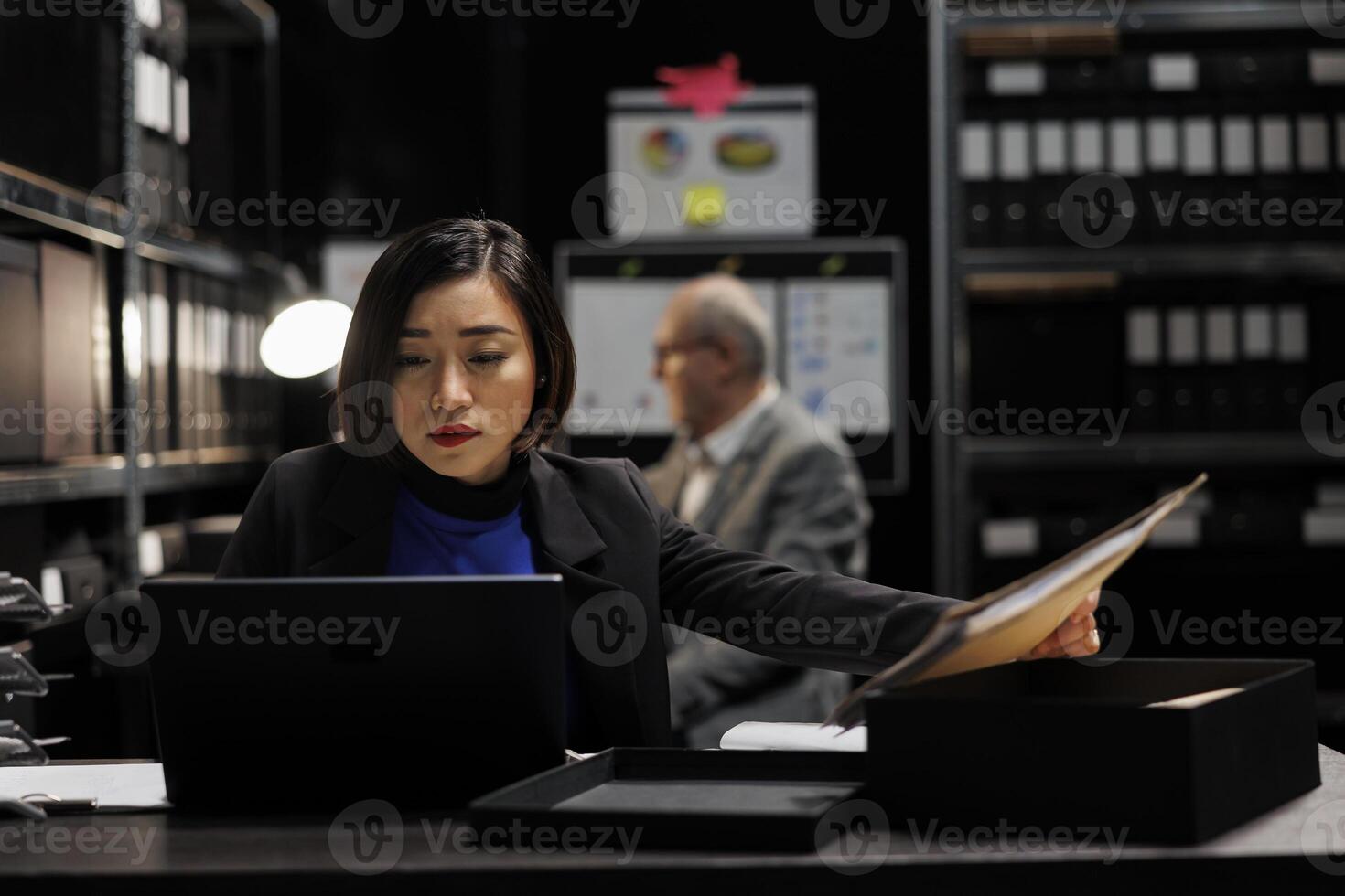 Asian private investigator starting criminal investigation case, comparing criminal investigation details. Detective woman in archive file cabinet office filled with criminology folders photo