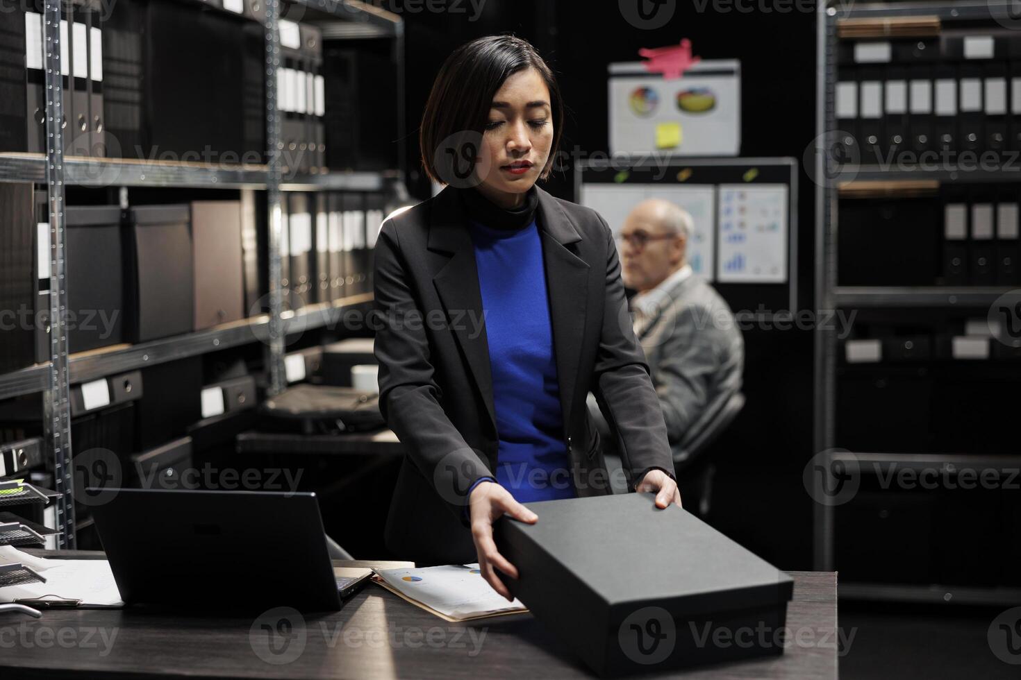 Asian manager bookkeeper storing annual profit revenue paperwork before official business inspection. Bureaucratic workplace filled with graphic charts and file folders on shelves photo