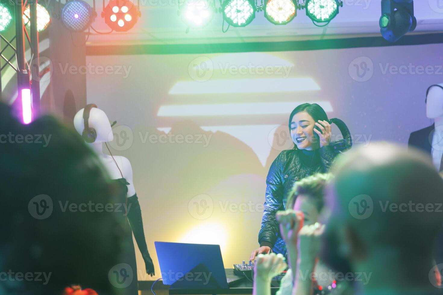 Dj mixing electronic music on stage with spotlights at discotheque party in nightclub. Asian using controller console during live performance concert while crowd dancing in club photo