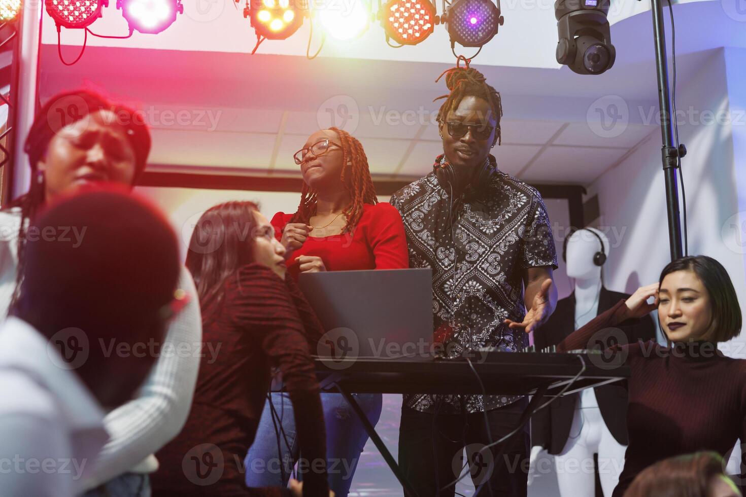 Band performing on stage illuminated with vibrant spotlights while tired people relaxing in nightclub. Young musicians playing while exhausted clubbers friends resting in club photo