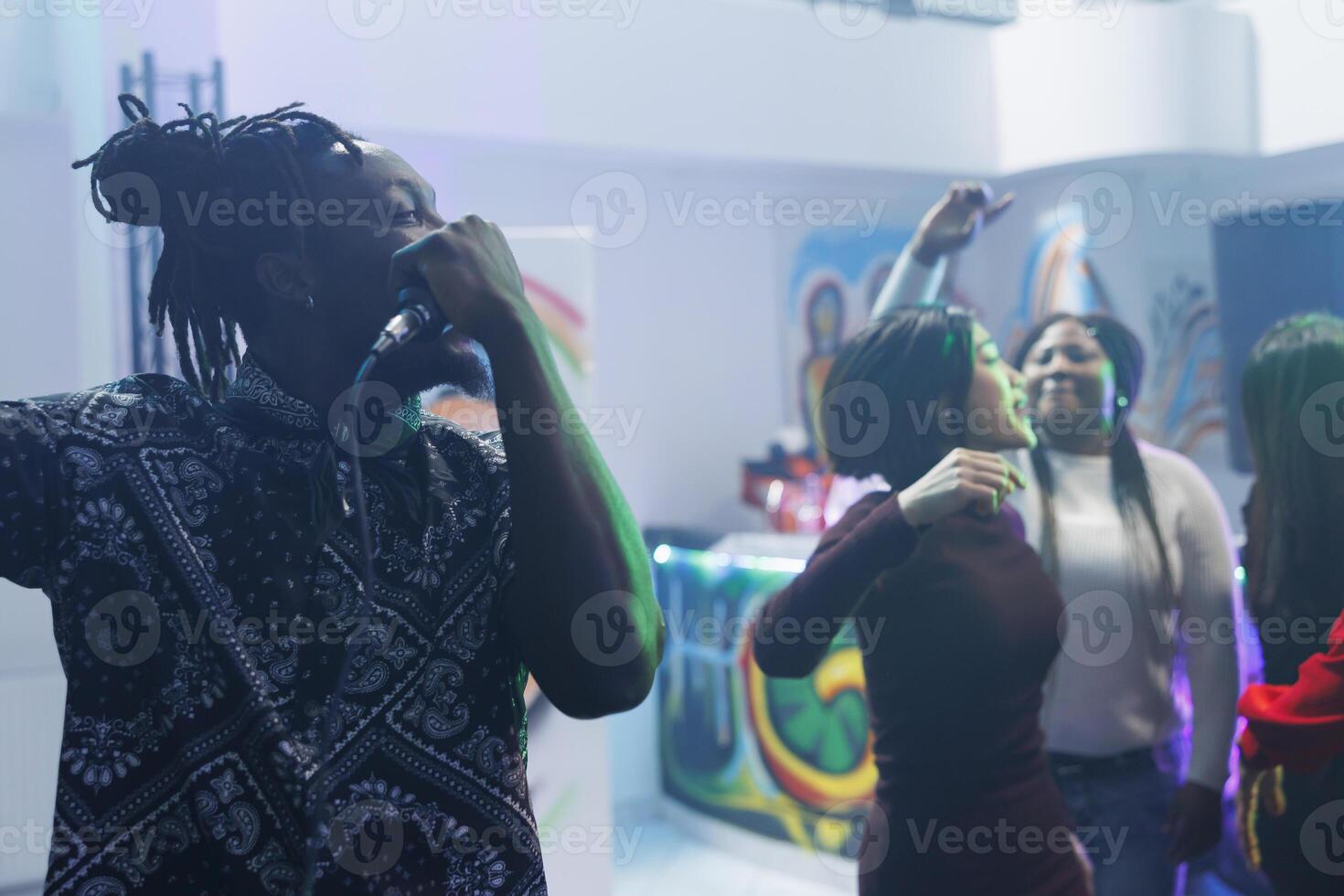 African american man singing in microphone while dancing with friends in crowded nightclub. Young clubber holding mic while clubbing partying at discotheque social gathering photo