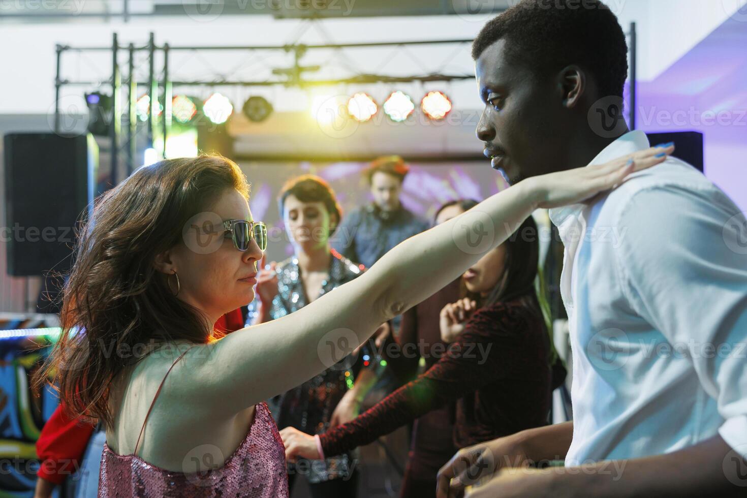 Young couple in love dancing while partying and relaxing in nightclub. Caucasian girlfriend and african american boyfriend making passionate moves on dancefloor while clubbing photo