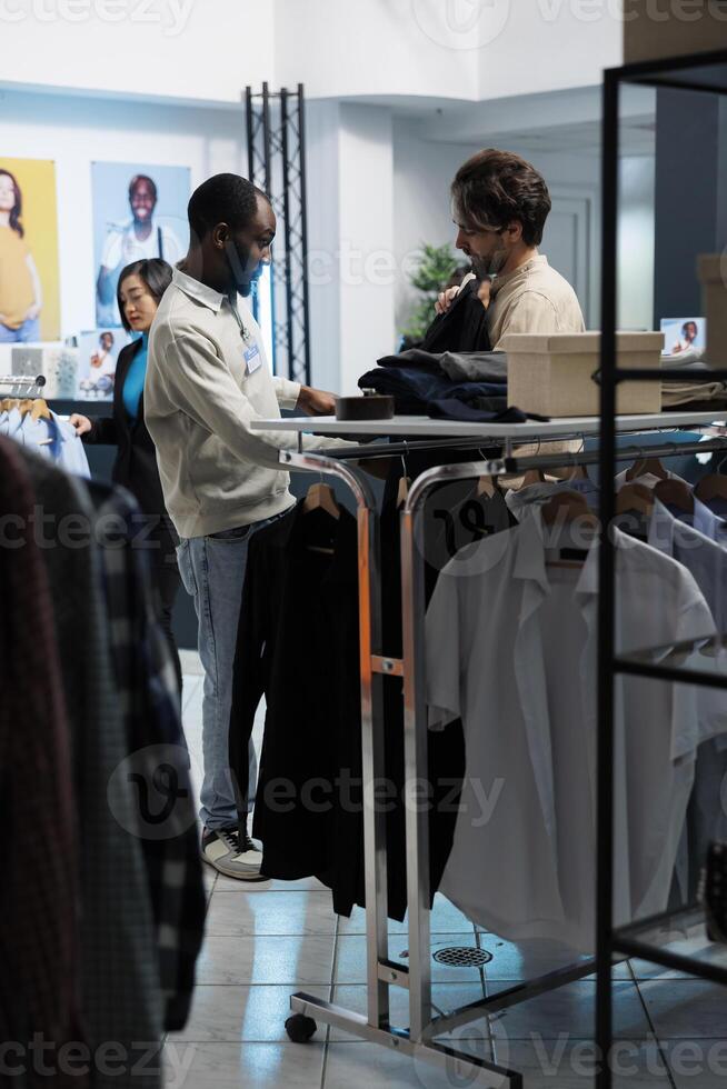 Clothing store employee assisting customer in selecting fashionable apparel, offering guidance on style. Boutique worker showcasing jacket to caucasian client and giving advice photo