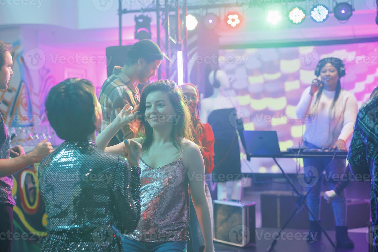 Girlfriends talking while relaxing on dancefloor at nightclub discotheque. Smiling women dancing together while partying and attending live electronic music concert in club photo