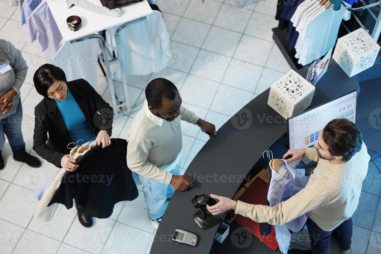 Cashier at clothing store checkout desk scanning and processing purchase for customer top view. Diverse people standing in line at counter desk while boutique employee using scanner photo