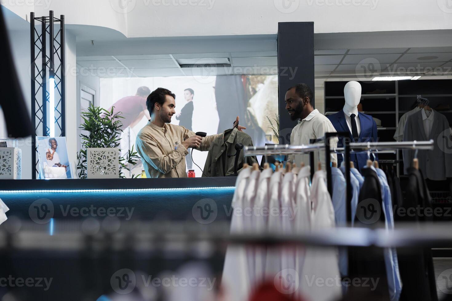 African american customer standing at clothing store counter while cashier scanning apparel. Man waiting at cash register desk and purchasing garment while shopping in boutique photo