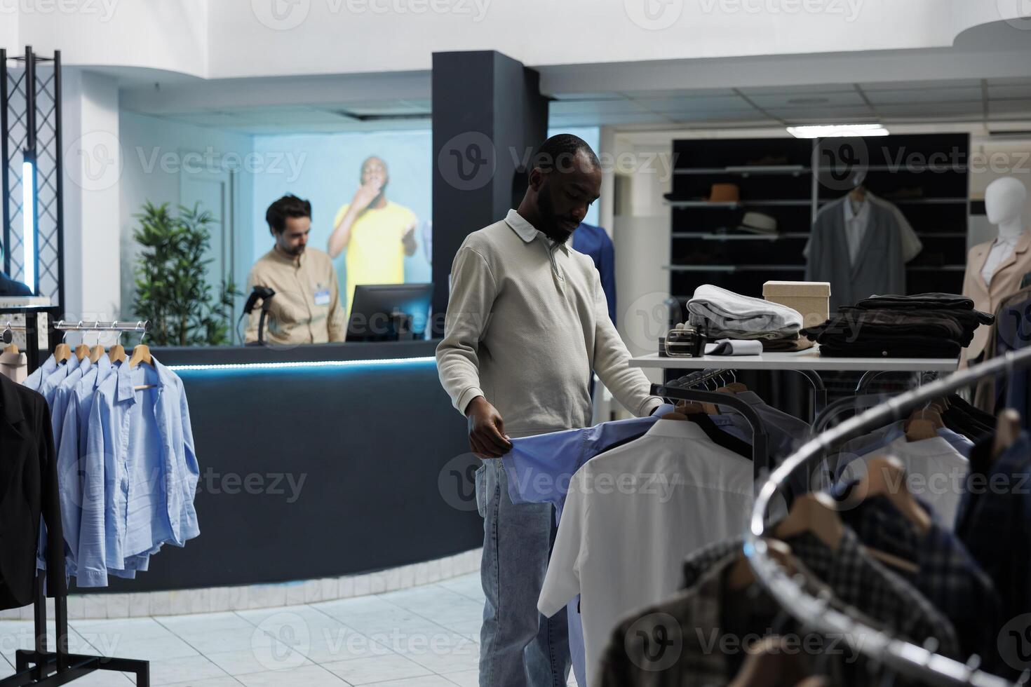 Clothing store client looking at casual shirt, examining style and fabric quality before buying. African american man browsing through apparel rack while shopping in fashion boutique photo