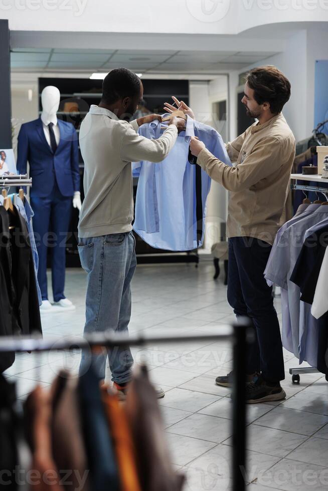 African american man selecting formal outfit and asking clothing store assistant for advice. Shopping mall boutique employee and customer discussing shirt and tie style match photo