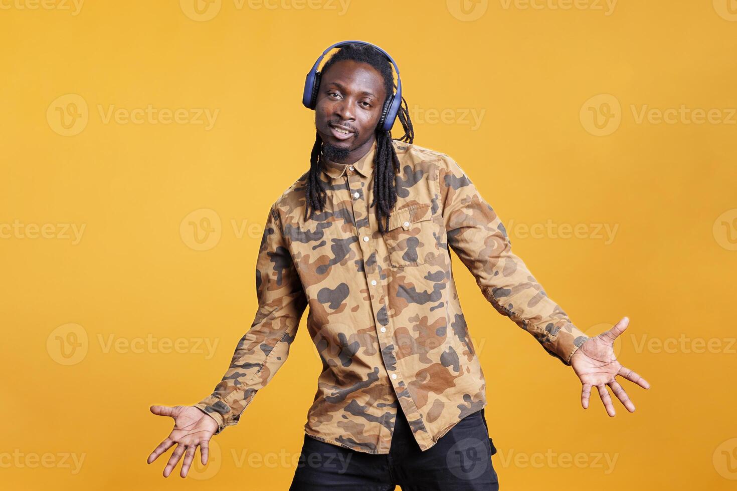 African american man wearing headphones enjoying music playlist having fun in studio over yellow background. Playful young adult listening radio song and dancing, enjoying free time photo