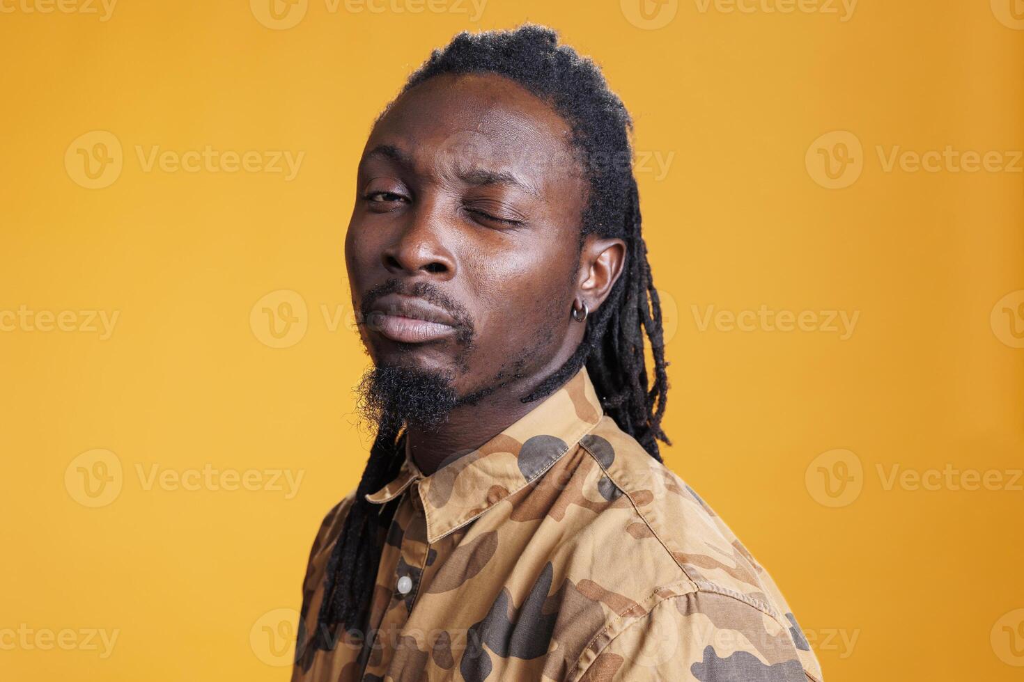 Cheerful confident african american man winking and fooling around over yellow background, doing eye wink on camera in studio. Positive playful young adult having fun, enjoying free time. photo