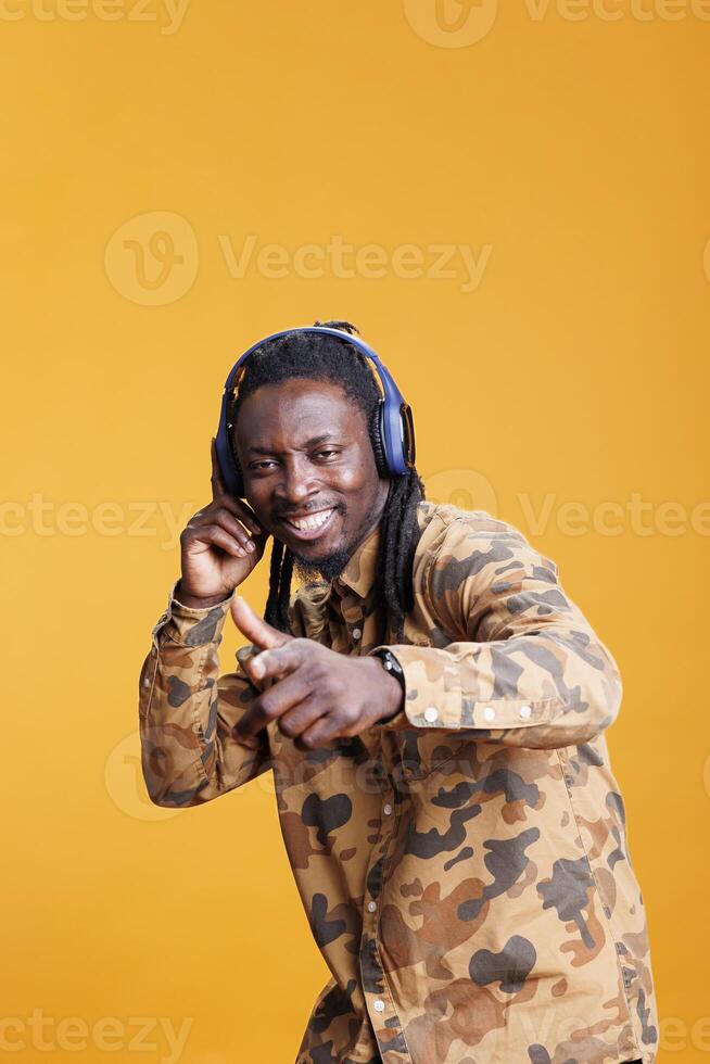 alegre joven adulto disfrutando radio canción en auriculares en estudio terminado amarillo fondo, bailando y teniendo divertido durante gratis tiempo. africano americano hombre relajante y escuchando a audio en cámara foto