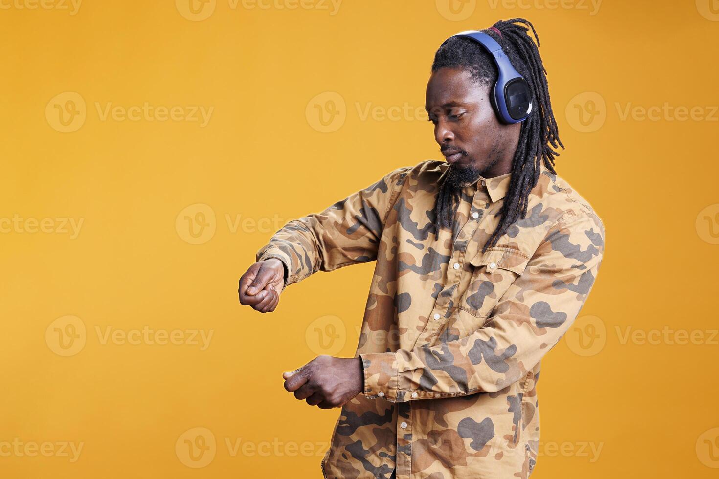 African american man dancing and vibing on favourite music in studio over yellow background, enjoying free time. Joyful adult wearing headset, having fun with dance while showing funny moves photo