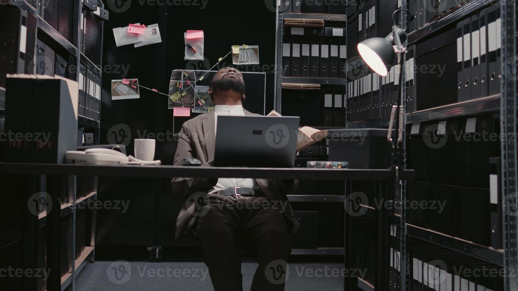 Male agent working with case information in evidence room, examining surveillance photos to uncover new clues. Police officer doing background checks for investigation. Handheld shot.