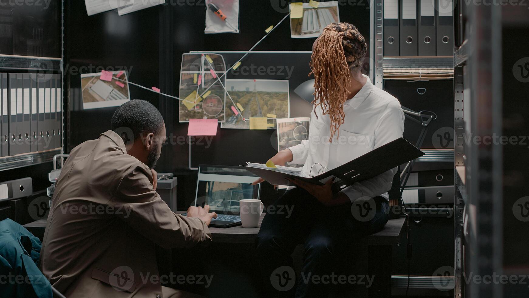 Two police officers looking at detective evidence map, investigators conducting investigation in incident room. Team of colleagues discussing about clues and identification photos. Handheld shot. photo