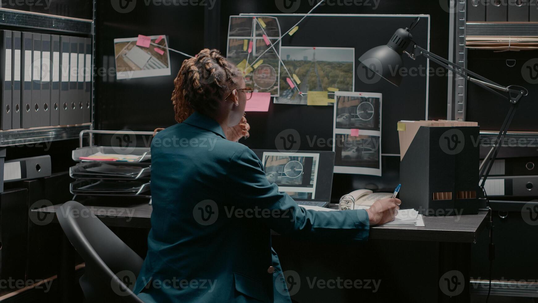 Police agent taking notes on case files in incident room, trying to solve criminal activity and catch suspect. Professional inspector examining research and surveillance photos. photo