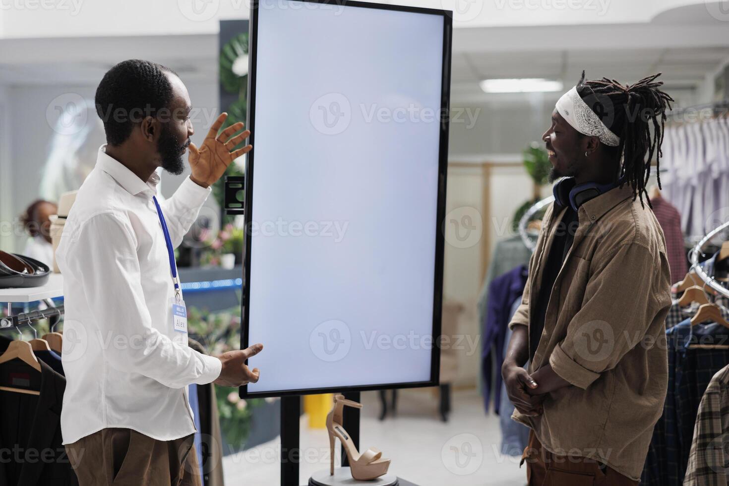 African american employee using smart display to assist customer with shoe purchase in shopping center. Clothing store showing promotion on whiteboard, helping customers selecting stiletto photo