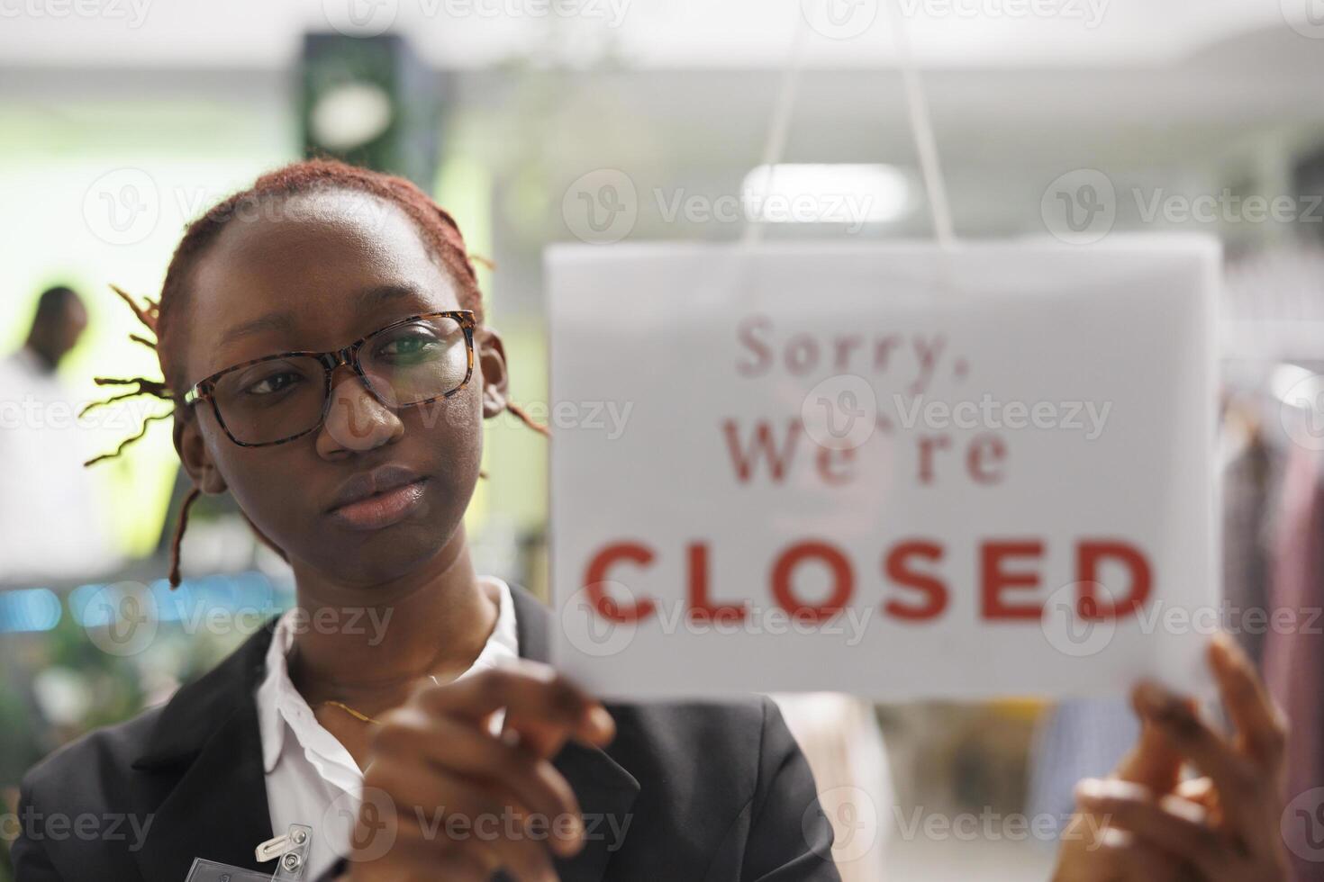 Clothing shop african american woman manager hanging sorry we are closed sign on window. Apparel mall department assistant holding sign noticing clients about end of business hours photo
