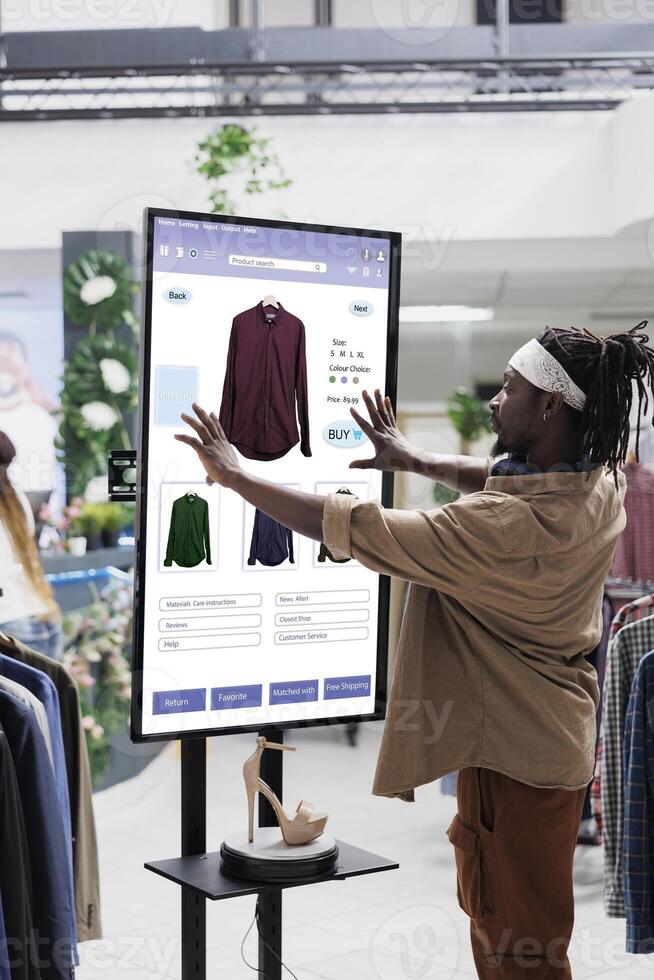 Online store buyer looks for clothes on touch screen board in clothing store, shopping for fashion items from self ordering kiosk display. Male client using interactive digital monitor. photo