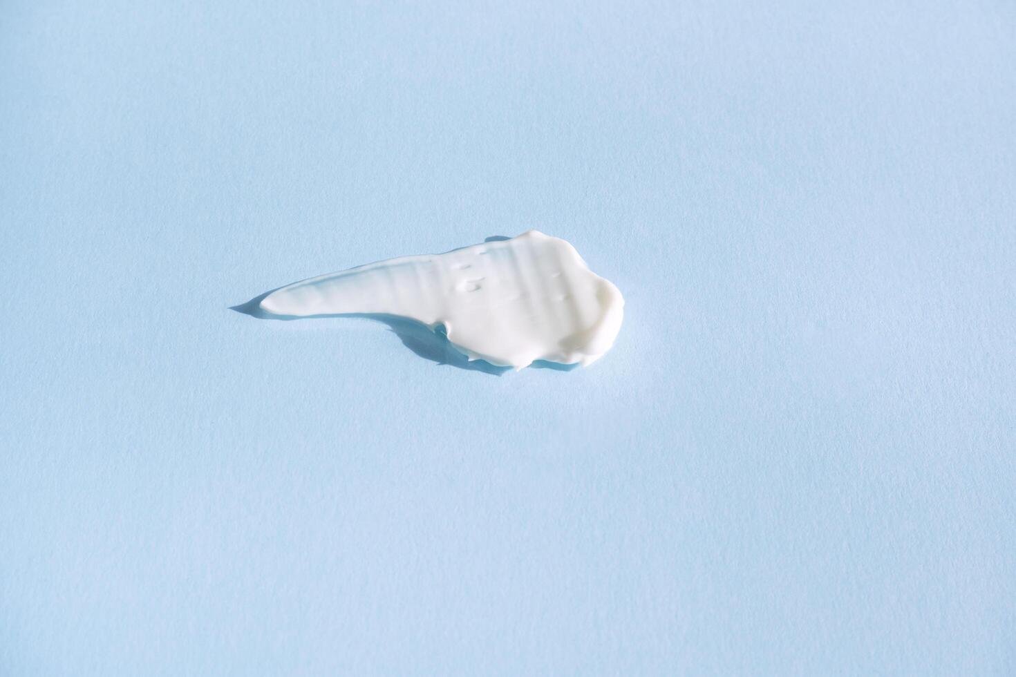 White smear of cosmetic cream on a blue background. Creamy base texture isolated. A smear of face cream. Close-up of creamy texture photo