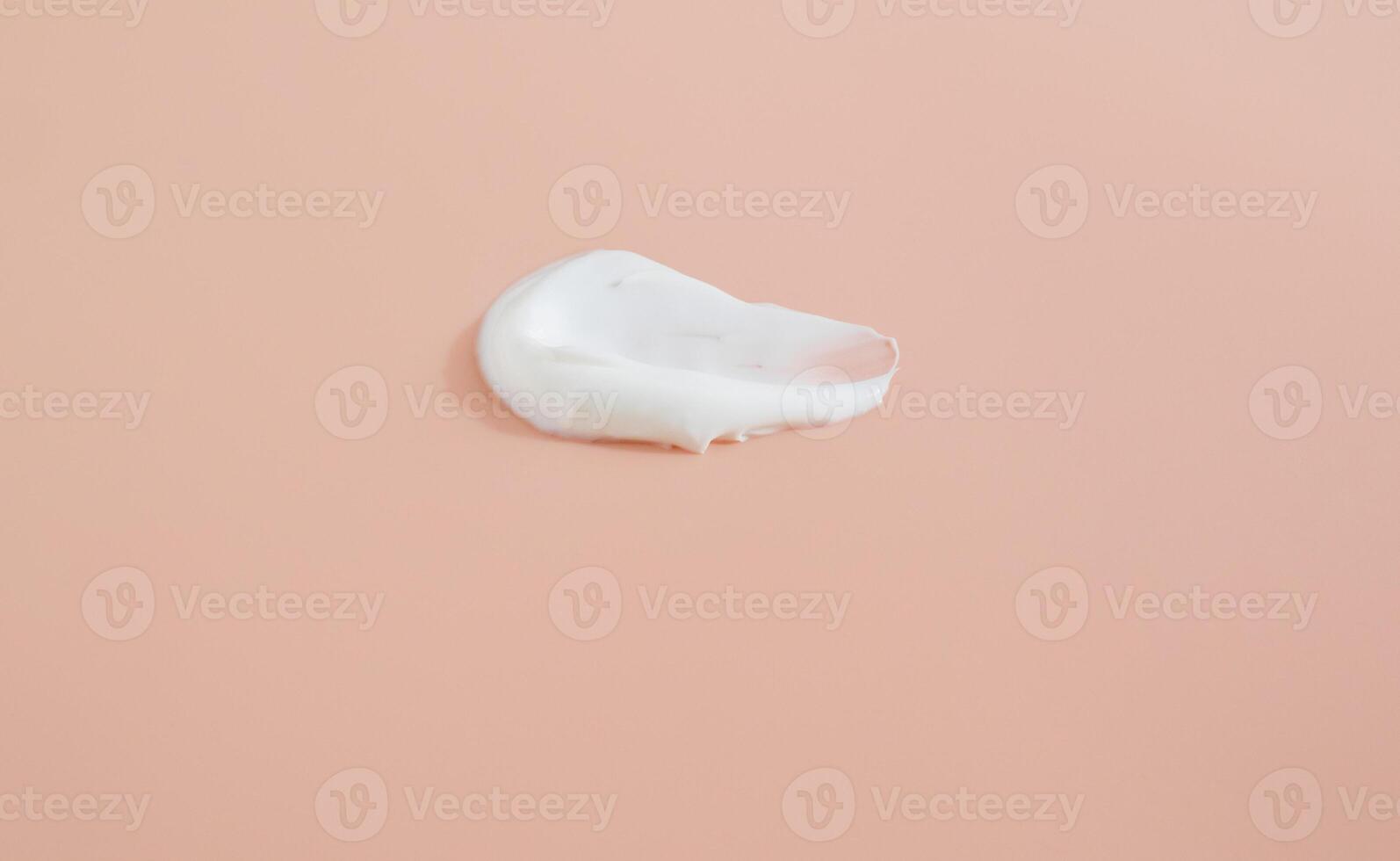 White smear of cosmetic cream on a beige background. Creamy foundation texture isolated. Smear of face cream. Close up of cream texture photo