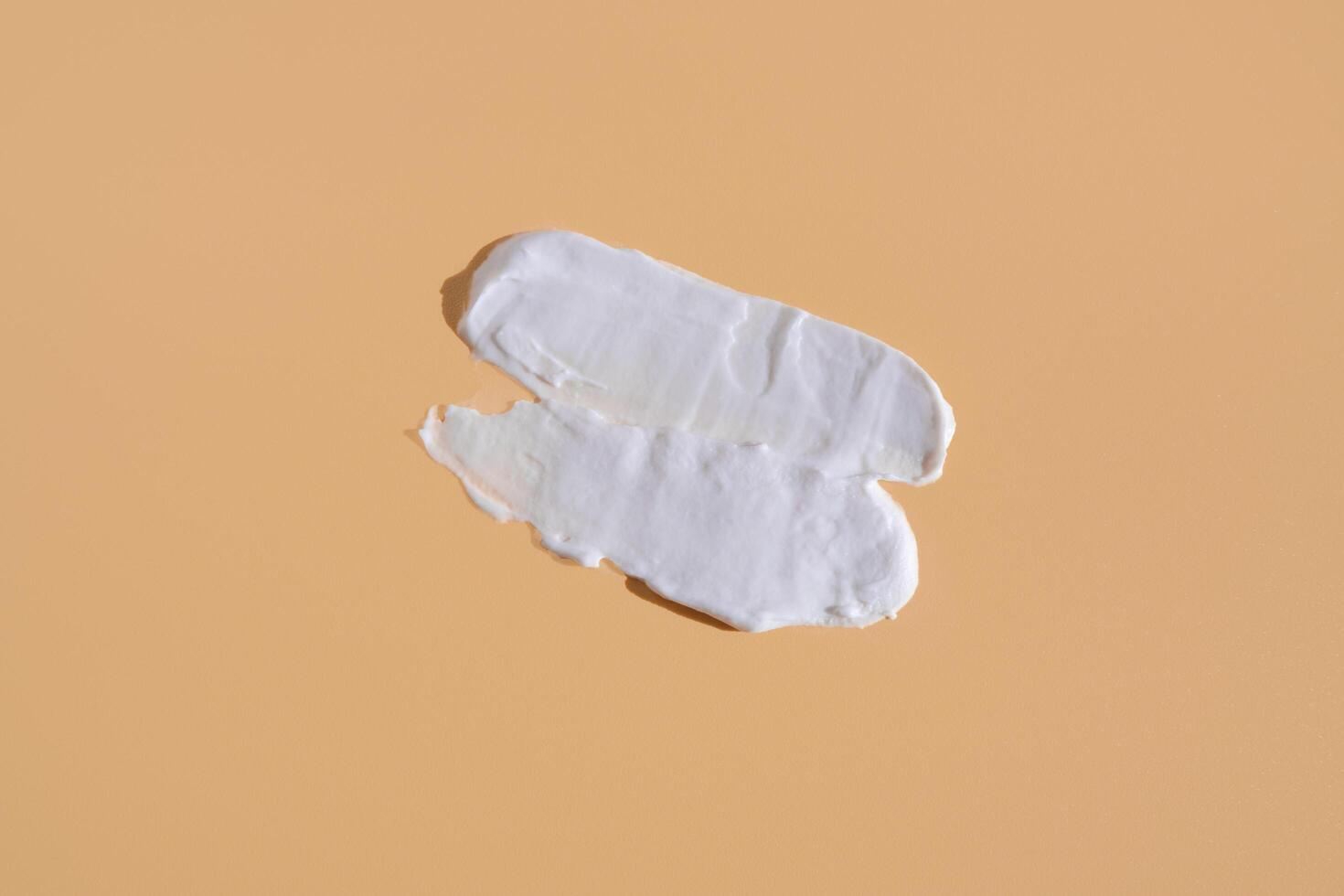 White smear of cosmetic cream on a beige background. Creamy foundation texture isolated. Smear of face cream. Close up of cream texture photo