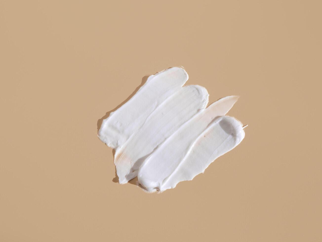 White smear of cosmetic cream on a beige background. Creamy foundation texture isolated. Smear of face cream. Close up of cream texture photo