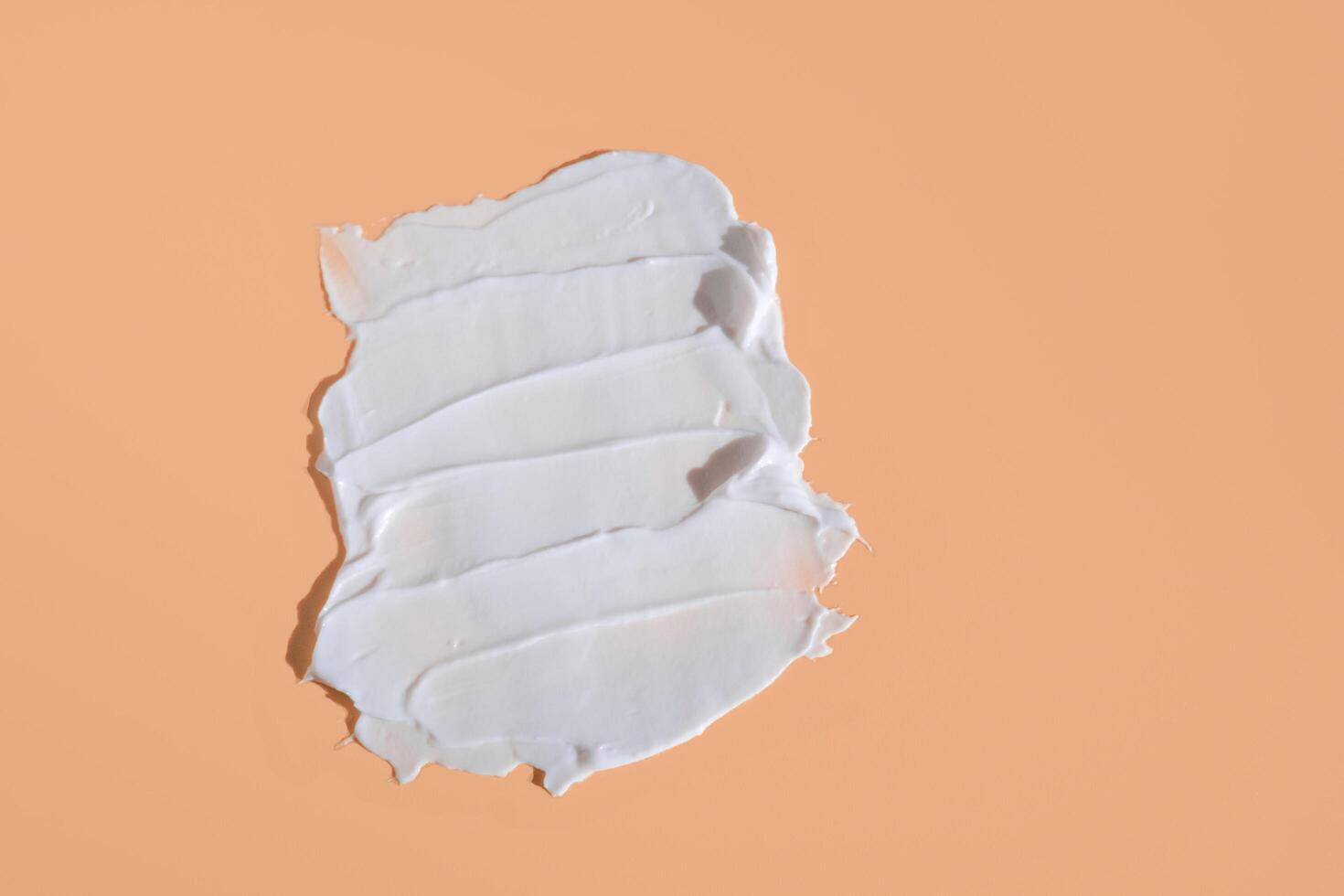 White smear of cosmetic cream on a beige background. Creamy foundation texture isolated. Smear of face cream. Close up of cream texture photo