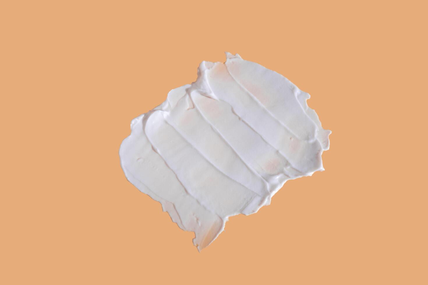 White smear of cosmetic cream on a beige background. Creamy foundation texture isolated. Smear of face cream. Close up of cream texture photo