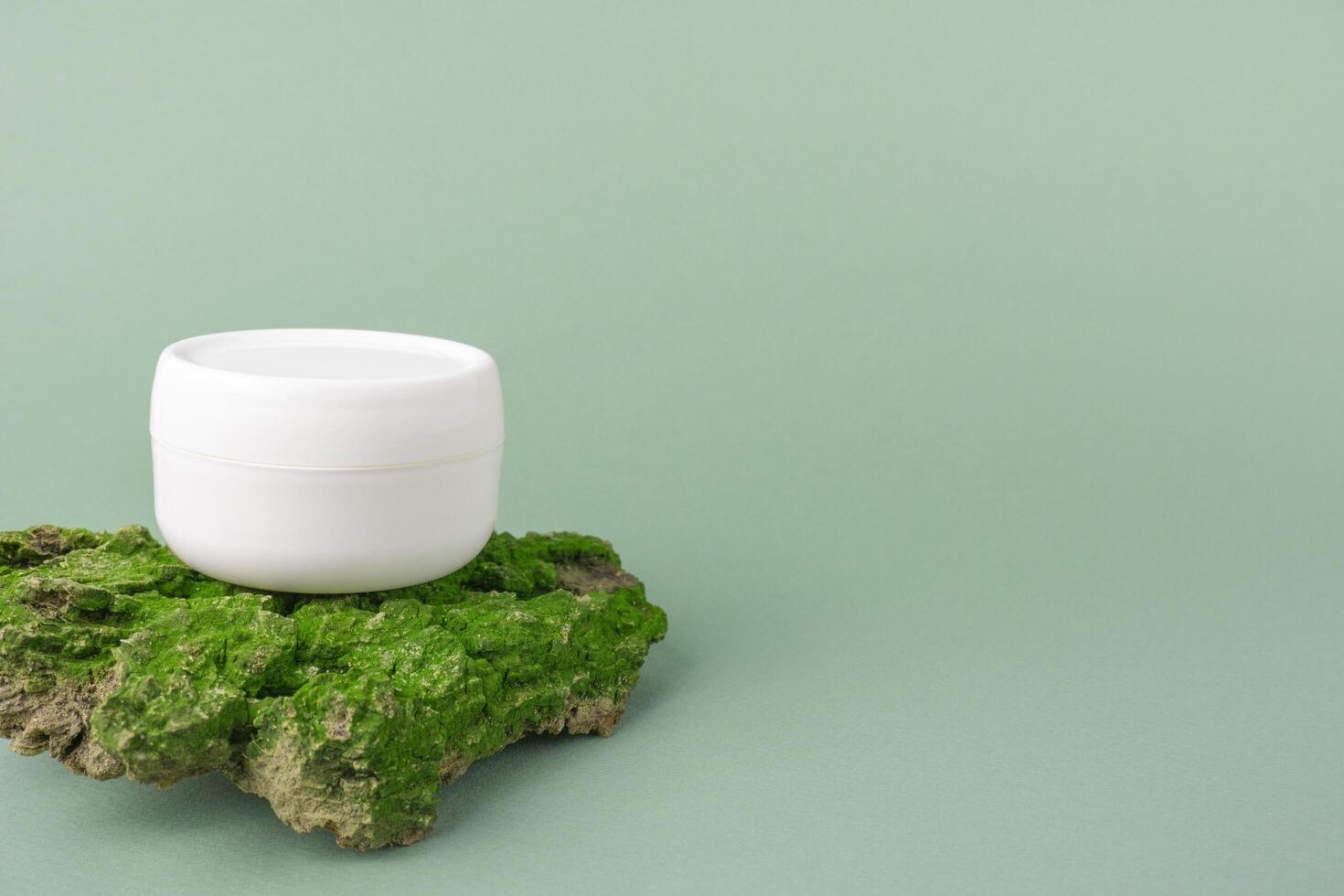 cuidado natural de la piel. cosméticos ecológicos. un frasco de crema facial en la corteza de un árbol con musgo verde sobre un fondo verde. copie el espacio foto