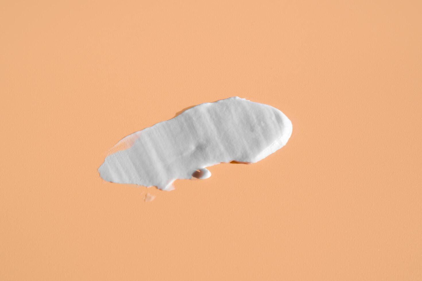 White smear of cosmetic cream on a beige background. Creamy foundation texture isolated. Smear of face cream. Close up of cream texture photo