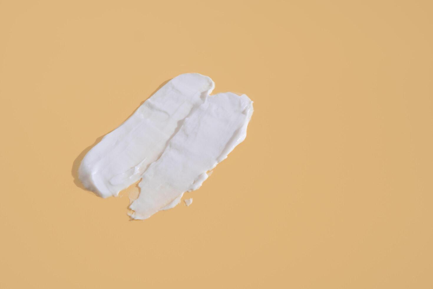 White smear of cosmetic cream on a beige background. Creamy foundation texture isolated. Smear of face cream. Close up of cream texture photo