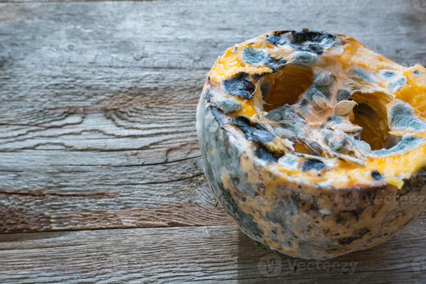 Orange moldy pumpkin on a wooden background. Mold and fungi on food, mold development, pests of stored vegetable products, a common problem. photo