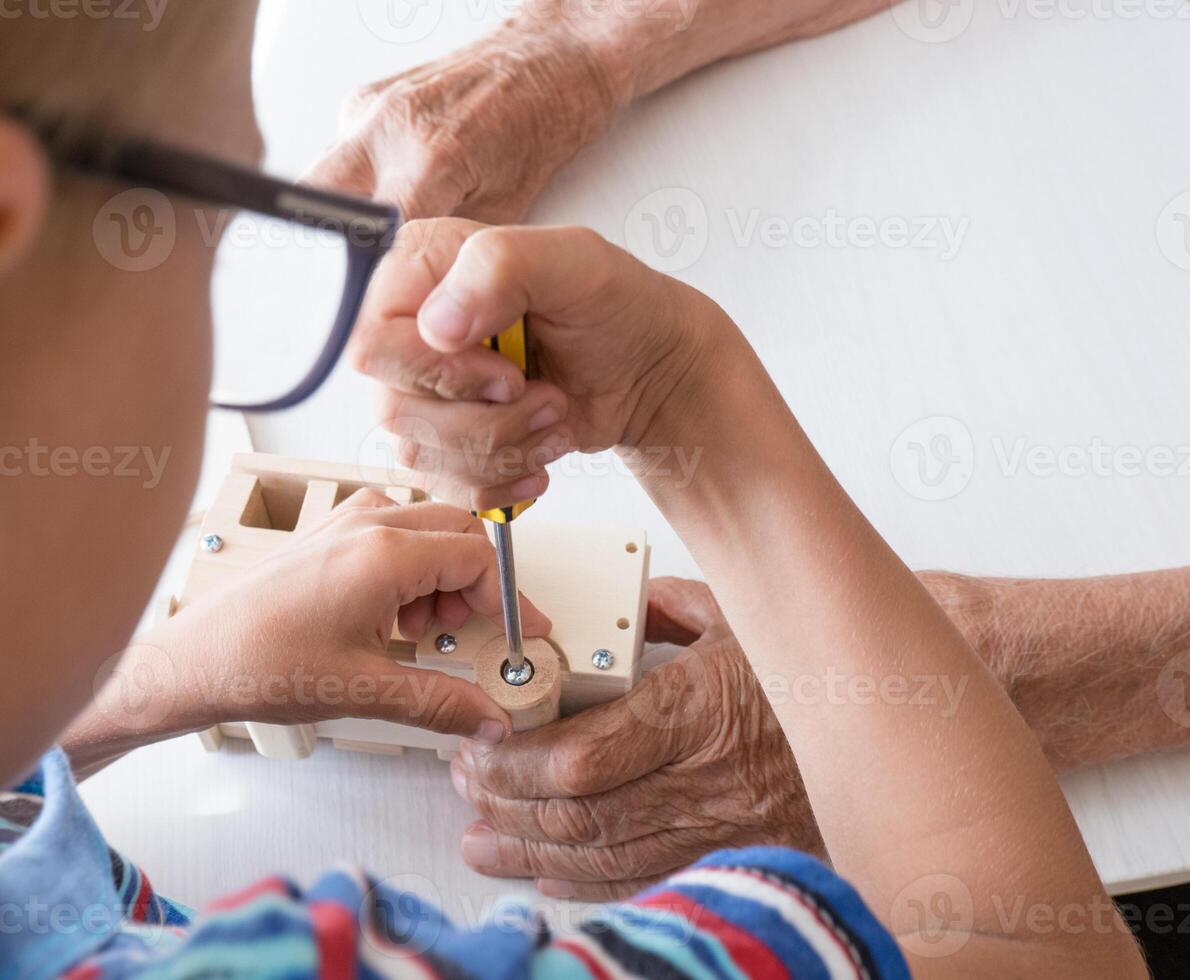 A five-year-old boy independently assembles a wooden construction kit with a screwdriver. Hands close-up. photo