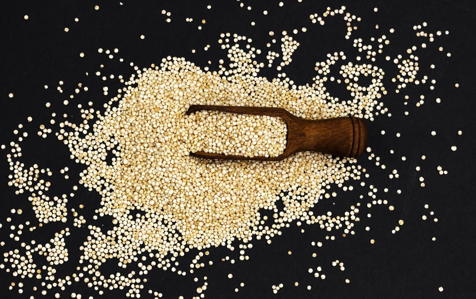 Quinoa seeds. Scoop of healthy white quinoa grains on black background, top view photo