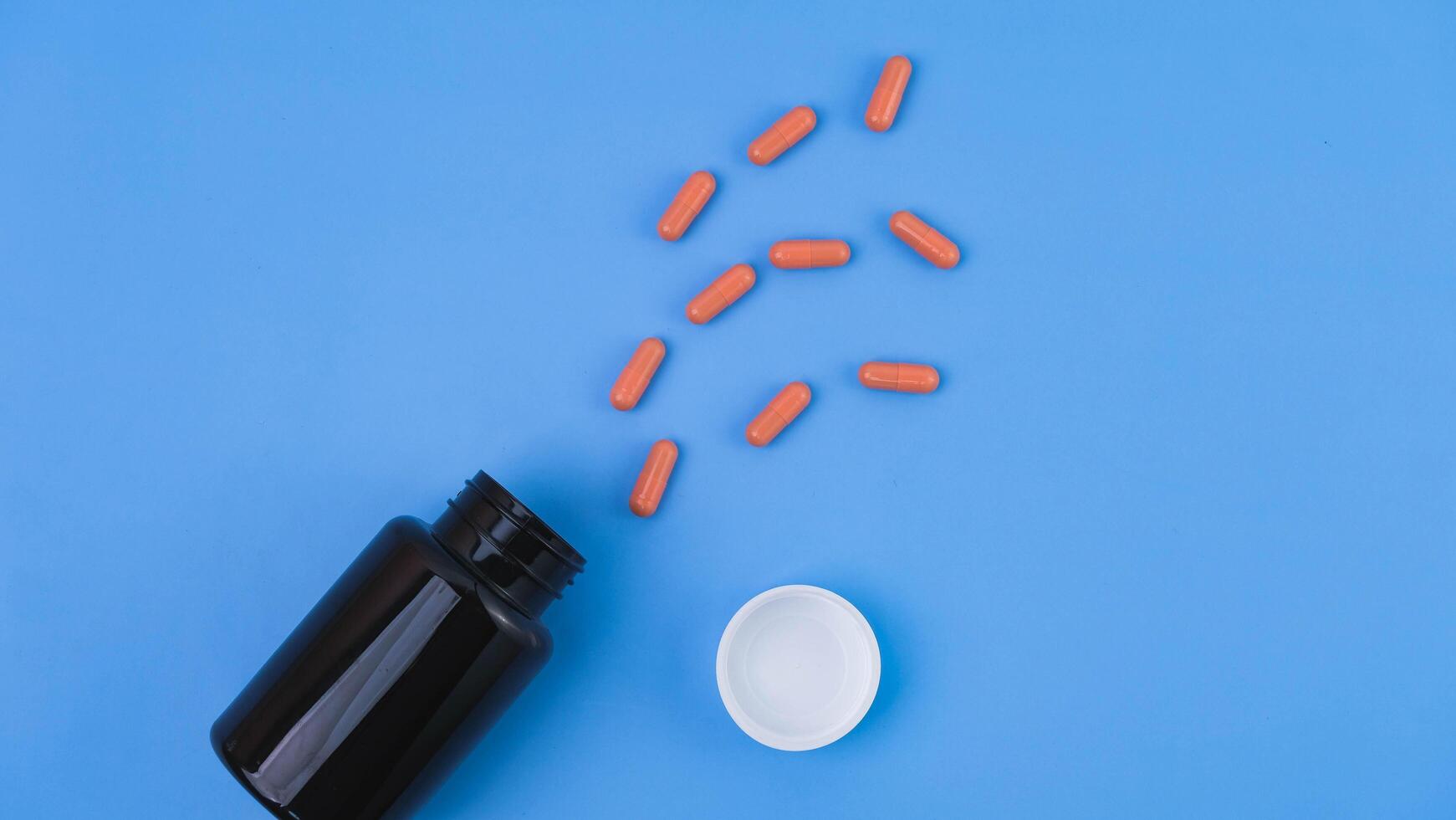 Pill capsule pouring from pharmacy bottle on blue background. Health care concept. photo