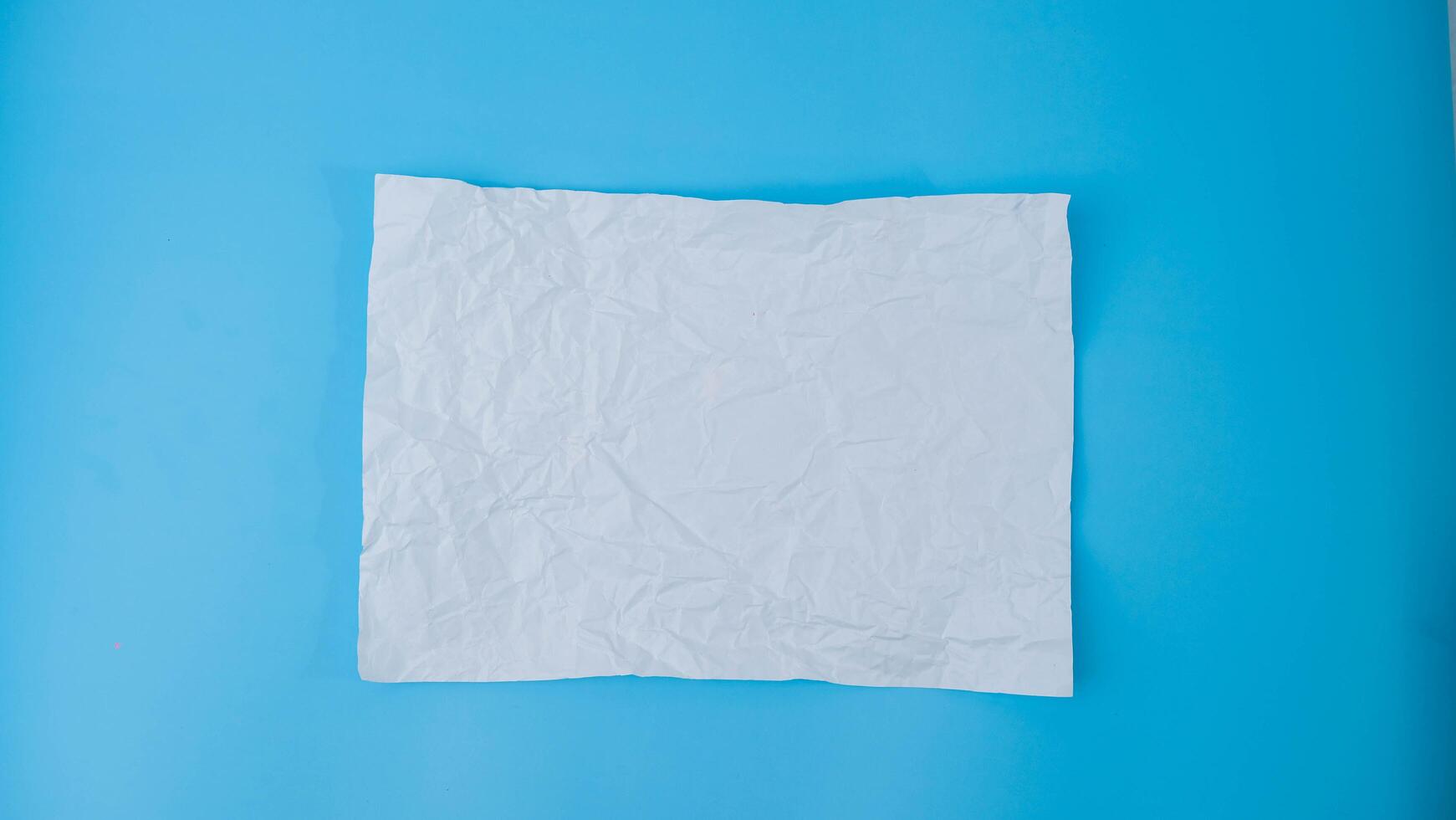 A paper ball is spread out into a blank sheet on blue background. Crumpled blank white paper with copy space for text or advertising space. photo
