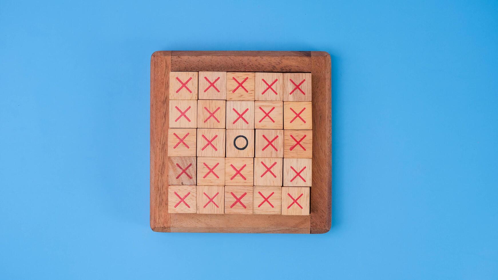 Wooden game board tic-tac-toe. Turning of the letters X-O and middle one different from each other on blue background. photo