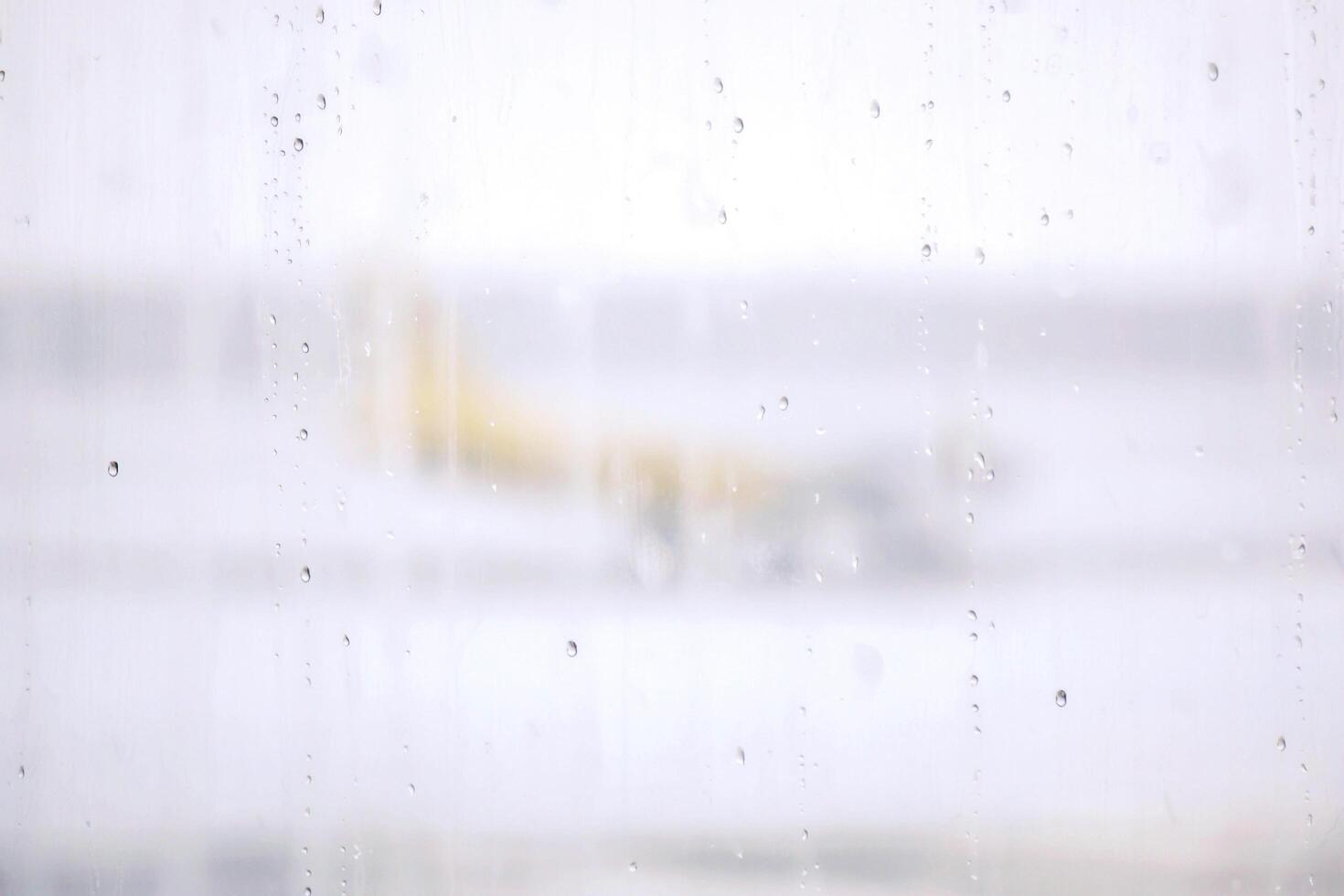 Raindrops on terminal airport's windows on blurry foggy and snowy outside with yellow plane on runway background. photo