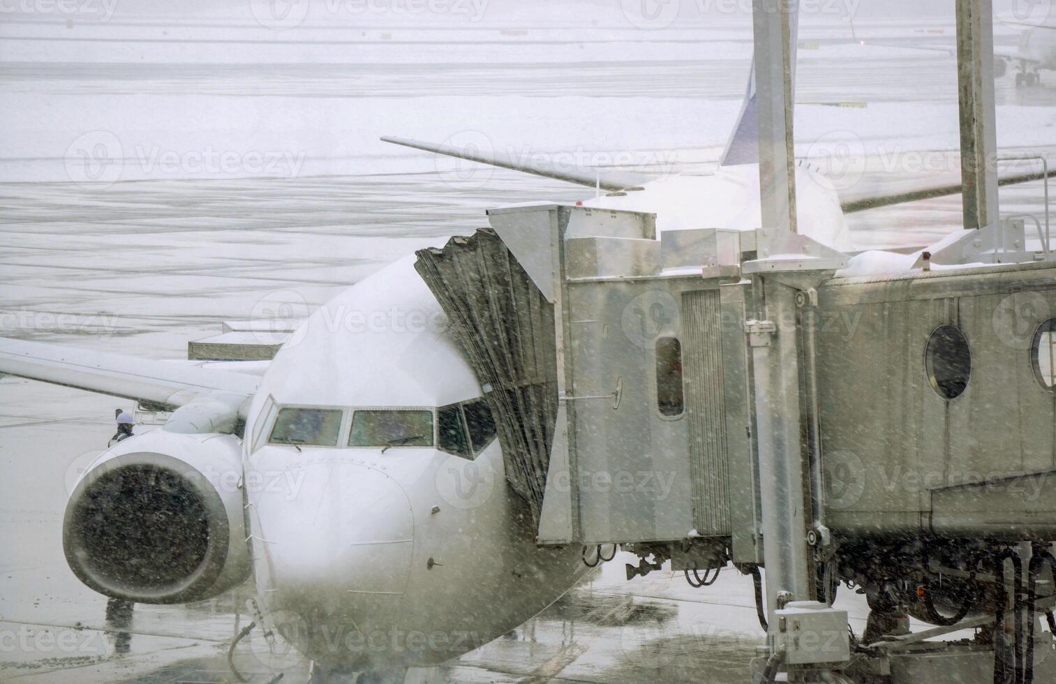 Closeup jet bridge and white airplane parked on airport ground and cotton snowing in winter weather. photo
