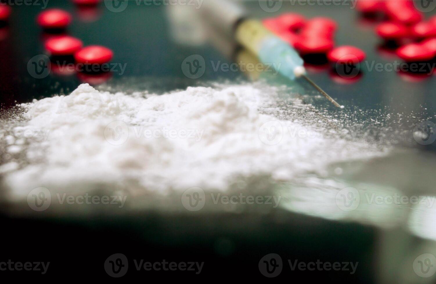 Closeup white powder front of plastic syringe and medical needle with red pills medicine on black background. Suppose to heroin and amphetamine with narcotic addiction. photo