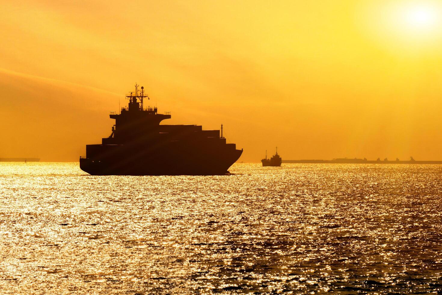 Silhouette of cargo ship with full shipload cargo containers are sailing in the Osaka bay evening with sun flare background. photo
